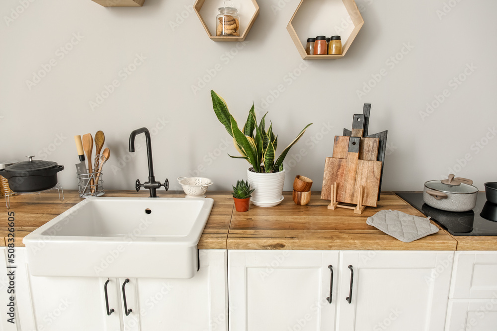 White counters with sink, food, kitchen utensils and houseplants near light wall