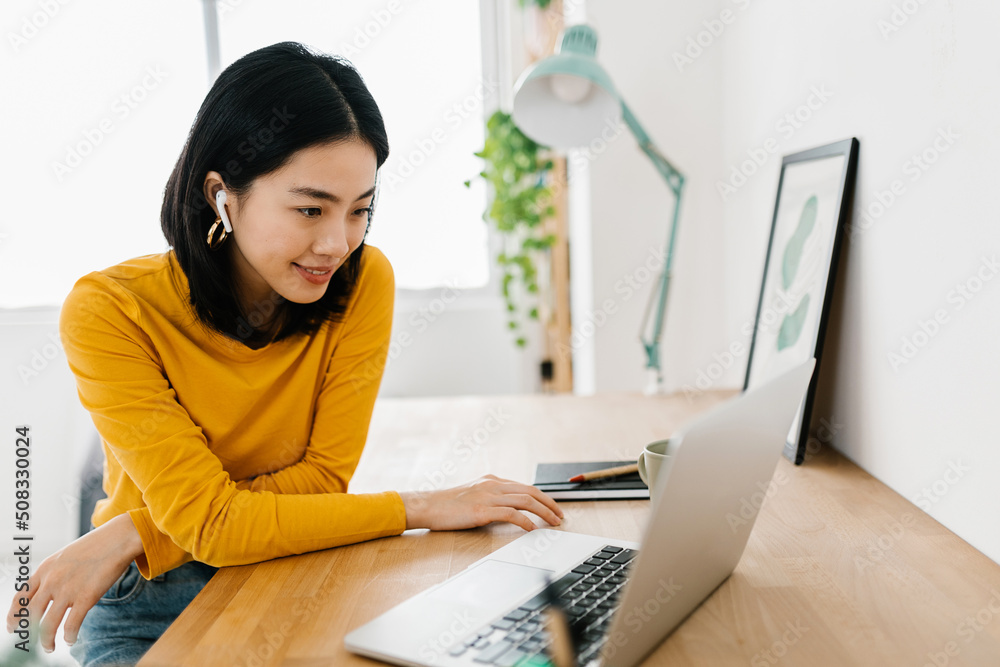 Smiling young asian teen girl wearing headphones having a video call on  laptop. Happy chinese pretty woman student looking at computer screen  watching webinar or doing video chat by webcam Stock-Foto