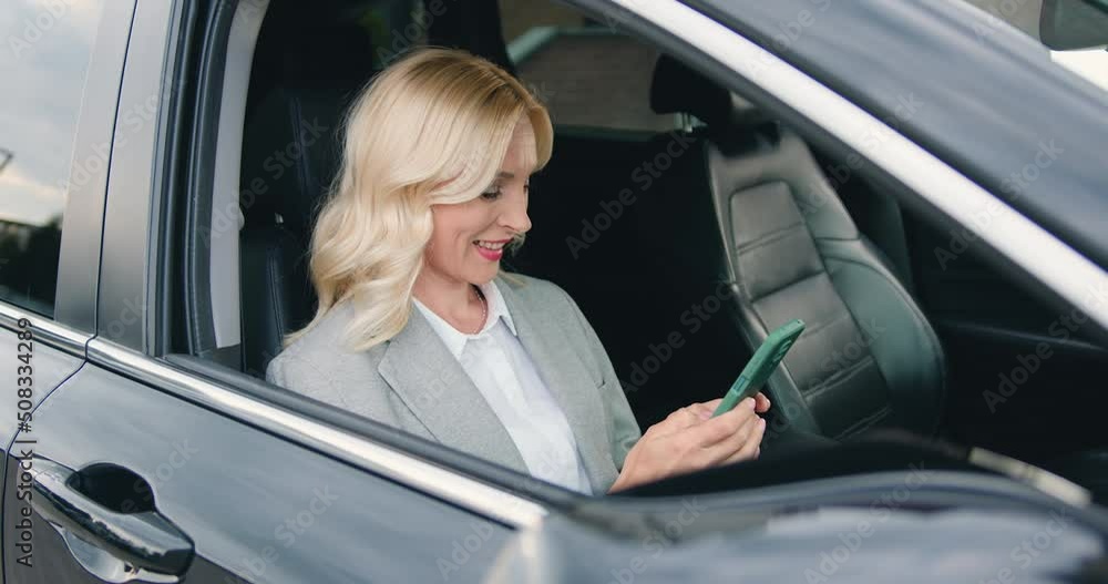 Businesswoman sitting on frontseat of car and using smartphone. Close up of attractive caucasian woman in car checking social media or the news on mobile phone or sending message Businesswoman sitting on frontseat of car and using smartphone. Close up of attractive caucasian woman in car checking social media or the news on mobile phone or sending message