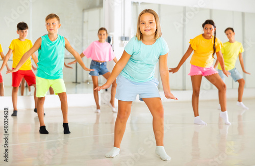 Portrait of cheerful preteen girl learning dynamic Charleston in choreographic studio for children.