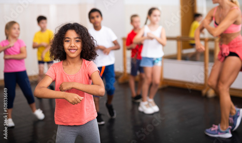Cute smiling preteen girl exercising with group of children in choreography class..