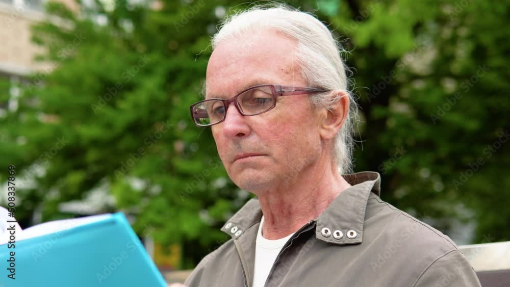 An elderly man with glasses reading a book on a park bench An elderly man with glasses reading a book on a park bench