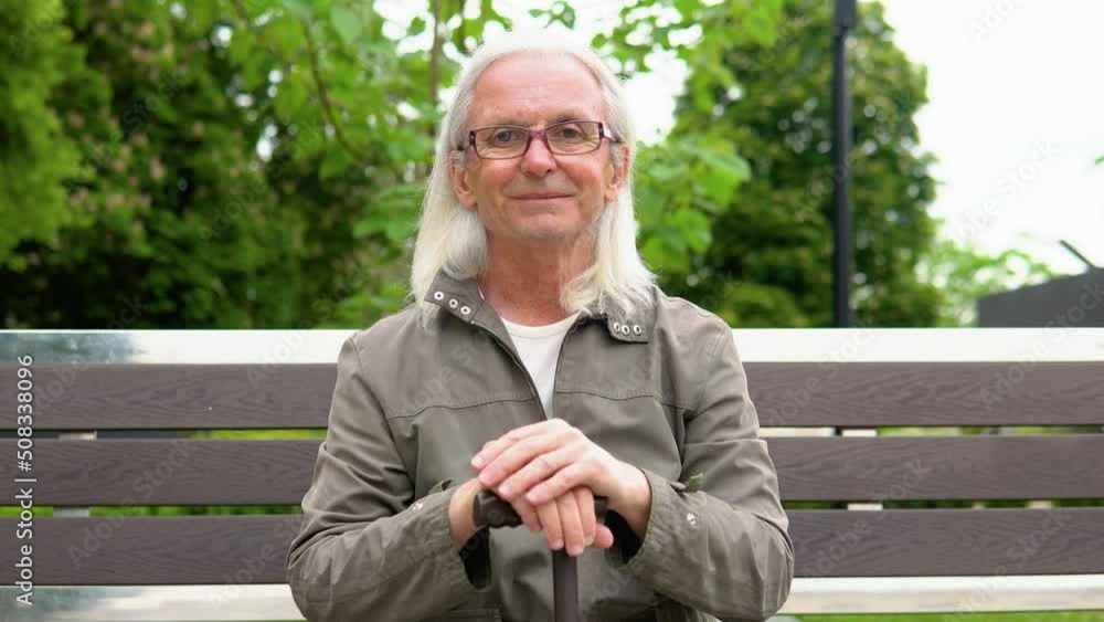 Portrait of elderly man smiling on bench in public city park. Happy senior man looking at camera Portrait of elderly man smiling on bench in public city park. Happy senior man looking at camera