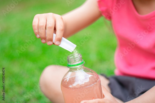 Drink with electrolytes in a transparent bottle in the hands of a happy child on a green lawn in a pink T-shirt photo