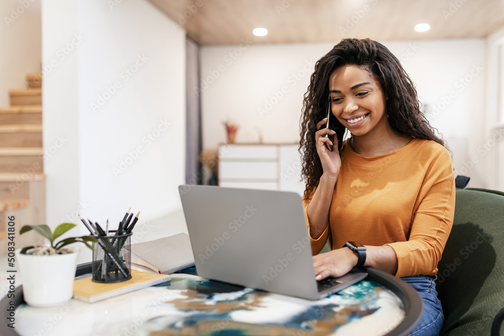 © Prostock-studio - Smiling black woman working and talking on phone at home