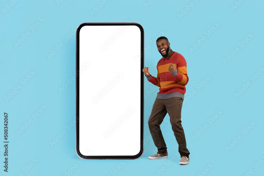 Great Offer. Overjoyed Black Man Celebrating Success Near Big Blank Smartphone Great Offer. Overjoyed Black Man Celebrating Success Near Big Blank Smartphone