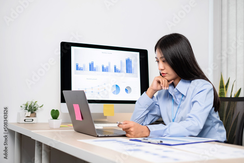 Asian woman working on a laptop with a cheerful and happy smile while working at the office