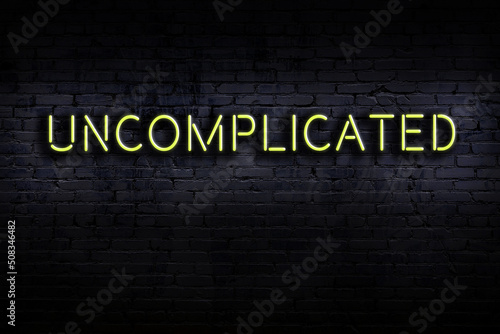 Night view of neon sign on brick wall with inscription uncomplicated