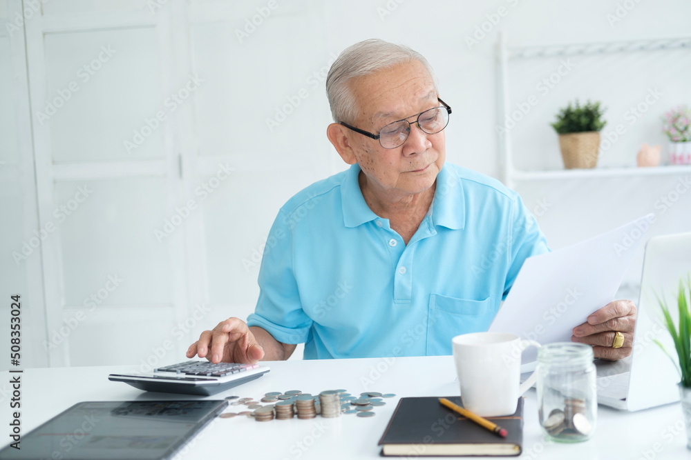 Serious man sitting at table near utility bill and calculating expenses