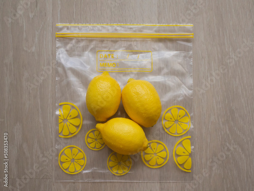 Trio of fresh lemons placed on a food storage ziplock bag on a light wood background