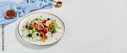 Classic greek salad with pesto sauce on ceramic plate. Vegetable salad with tomatoes, cucumber, paprika, onion and olives. Traditional grecian food. Greek salad on concrete background.