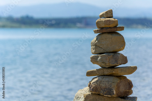 Rock cairn the art of stone balancing on a stone near a blue water flowing lake. Sunny day on the lake. A mood of calm and harmony with nature.