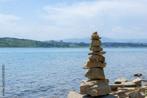 Rock cairn the art of stone balancing on a stone near a blue water flowing lake. Sunny day on the lake. A mood of calm and harmony with nature.
