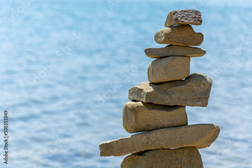 Rock cairn the art of stone balancing on a stone near a blue water flowing lake. Sunny day on the lake. A mood of calm and harmony with nature.