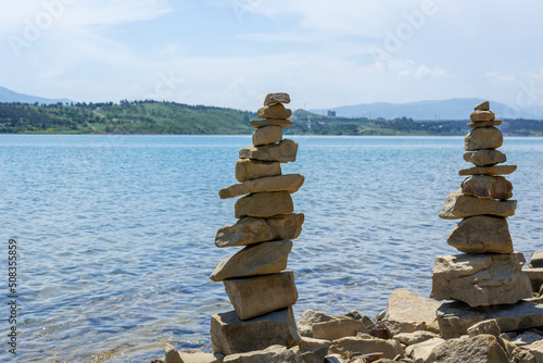 Rock cairn the art of stone balancing on a stone near a blue water flowing lake. Sunny day on the lake. A mood of calm and harmony with nature.