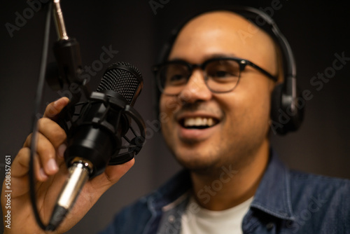 Young asian man host streaming podcast with condenser microphone work on laptop at small broadcast home studio. Content creator blogger recording voice over radio interview guest conversation