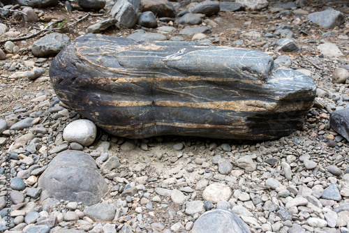 A large layered sedimentary river rock sits on the ground near the river