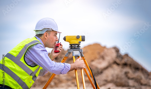 Surveyor engineer wearing safety uniform and helmet with equipment theodolite to measurement positioning on the construction site of the road with construct machinery background photo