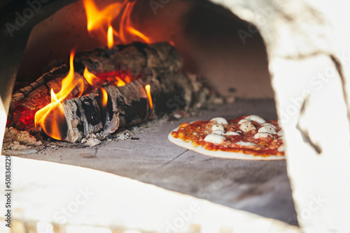 Pizza baking on the deck of a wood-fired oven. The process of making homemade pizza. The concept of homemade fast food. Front view.