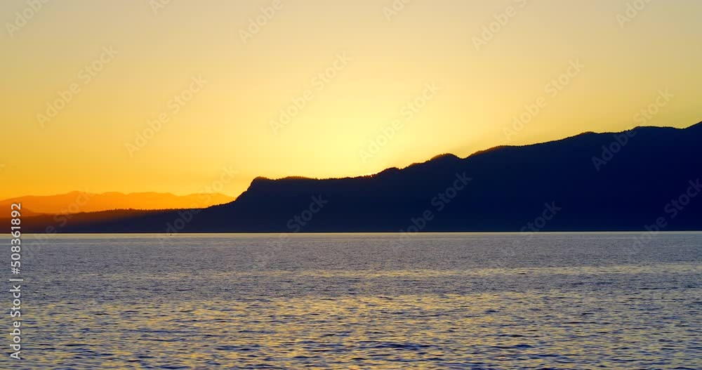 Establishing shot of ocean sunset over mountains in slow motion at summer day in Vancouver, Canada, North America. Evening time on September 2021. Still camera. ProRes 422 HQ. Establishing shot of ocean sunset over mountains in slow motion at summer day in Vancouver, Canada, North America. Evening time on September 2021. Still camera. ProRes 422 HQ.
