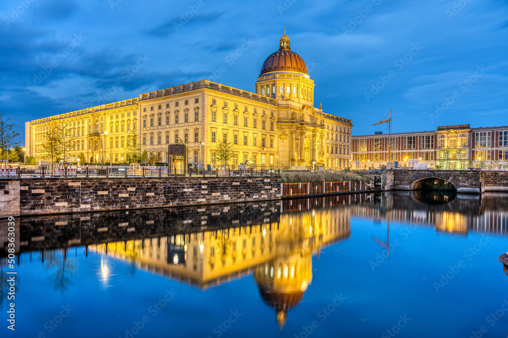 The imposing reconstructed City Palace in Berlin at night reflected in a small canal