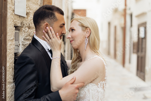 Young romantic couple, blond woman and black-haired man, looking at each other, bride holding groom face. Oath, promise