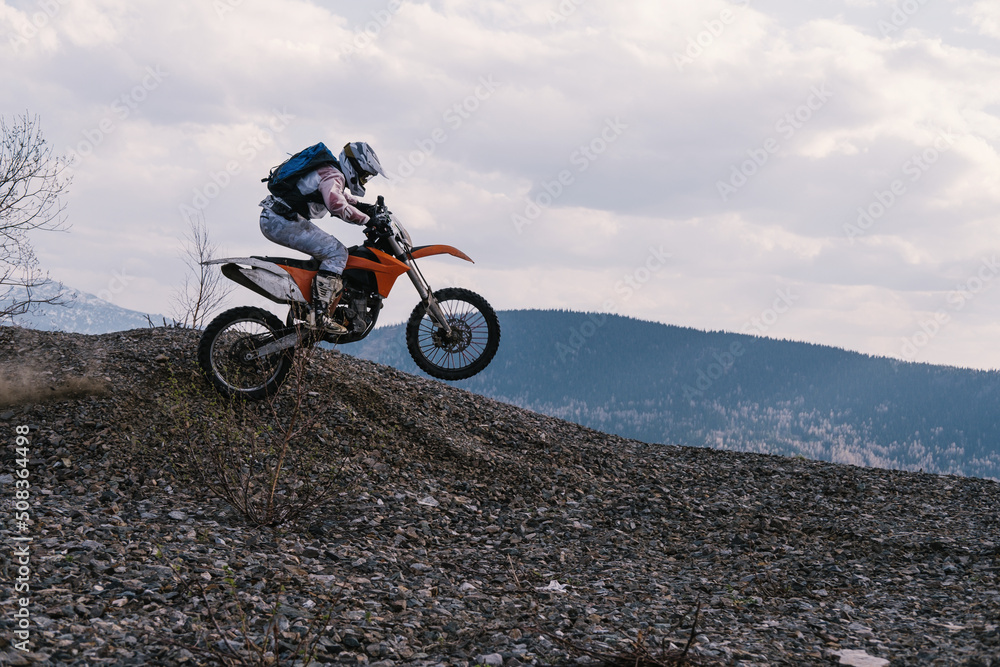 Obraz premium Motorcyclist jumping on dirt motorcycle on rubble mountain top with mountains view