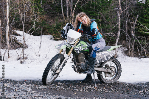 Portrait of attractive female sitting on dirt motorcycle off-road with snow on summer day