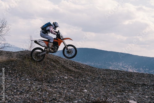 Motorcyclist jumping on dirt motorcycle on rubble mountain top with mountains view