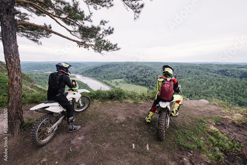 bikers friends resting on enduro motorcycle on the edge of cliff with gorgeous view of mountain view