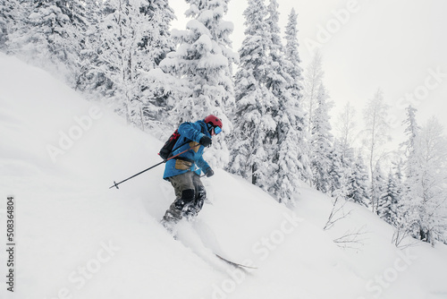 Skier moving in snow powder in forest on steep slope of ski resort. Freeride, winter sports outdoor