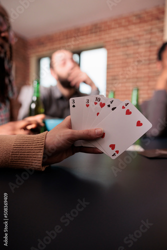 Close up shot of caucasian woman hand holding card games while enjoying fun leisure activity with friends. Person playing card games with people while having snacks and beverages.