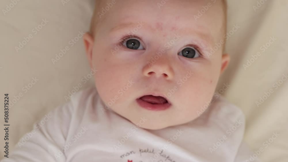 Cute six month old baby girl lies on the bed and looks at the camera and smiling, top view Cute six month old baby girl lies on the bed and looks at the camera and smiling, top view
