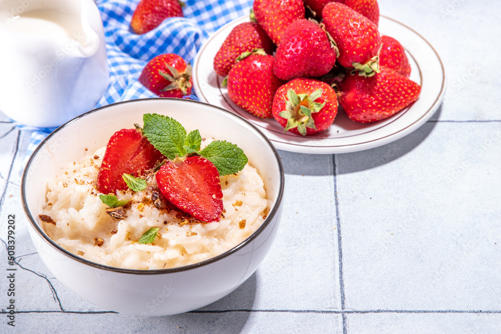 Rice porridge or pudding with fresh strawberry and nuts for breakfast, with plate of strawberries, white tiled background copy space Rice porridge or pudding with fresh strawberry and nuts for breakfast, with plate of strawberries, white tiled background copy space