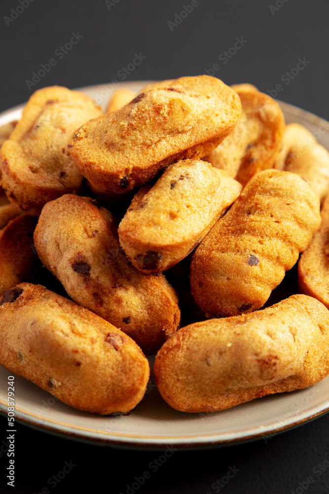 Homemade Chocolate Chips Madeleines on a Plate on a black background, side view. Close-up. Homemade Chocolate Chips Madeleines on a Plate on a black background, side view. Close-up.
