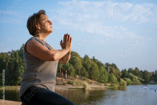 Lonely woman meditates sitting on shore lake with her palms clasped in front her or prays. The concept of relaxation and spiritual balance and connection with nature