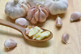 top view smashed garlic in a wooden spoon along with garlic bulbs and garlic cloves on wood background. Concept of spices for healthy cooking. Selected focus.