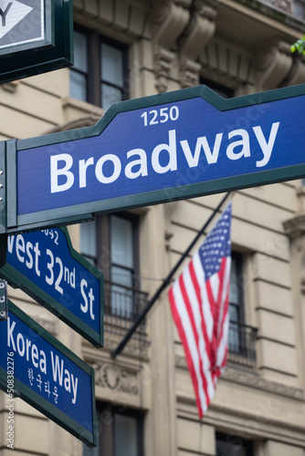 panneau de signalisation indiquant l'avenue de Broadway à New York, avec en arrière plan le drapeau américain et un building