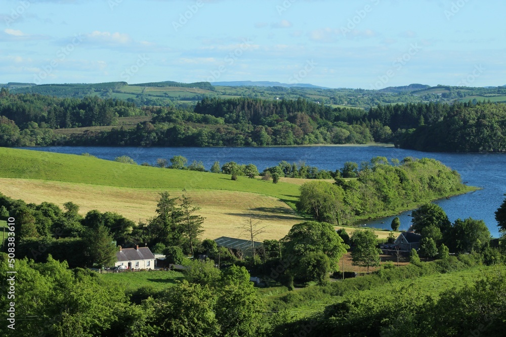 Landscape of rural County Leitrim, Ireland at shores of Lough Gill in summertime featuring cottage home nestled amongst fields of farmland pastures bordered by trees