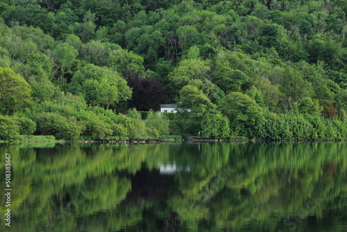 Cottage house nestled amongst greenery of trees in forest reflected in still waters of Lough Gill  situated in rural County Leitrim  Ireland