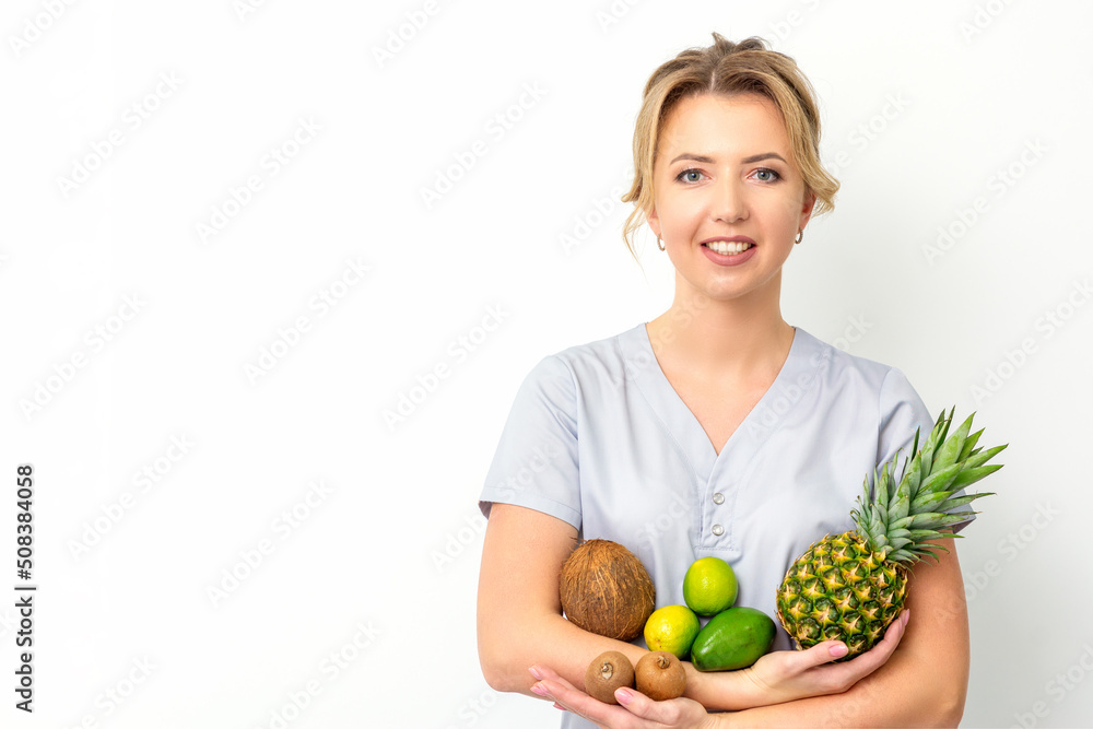 Portrait of a young caucasian smiling female nutritionist with different fruits in her hands over white background Portrait of a young caucasian smiling female nutritionist with different fruits in her hands over white background