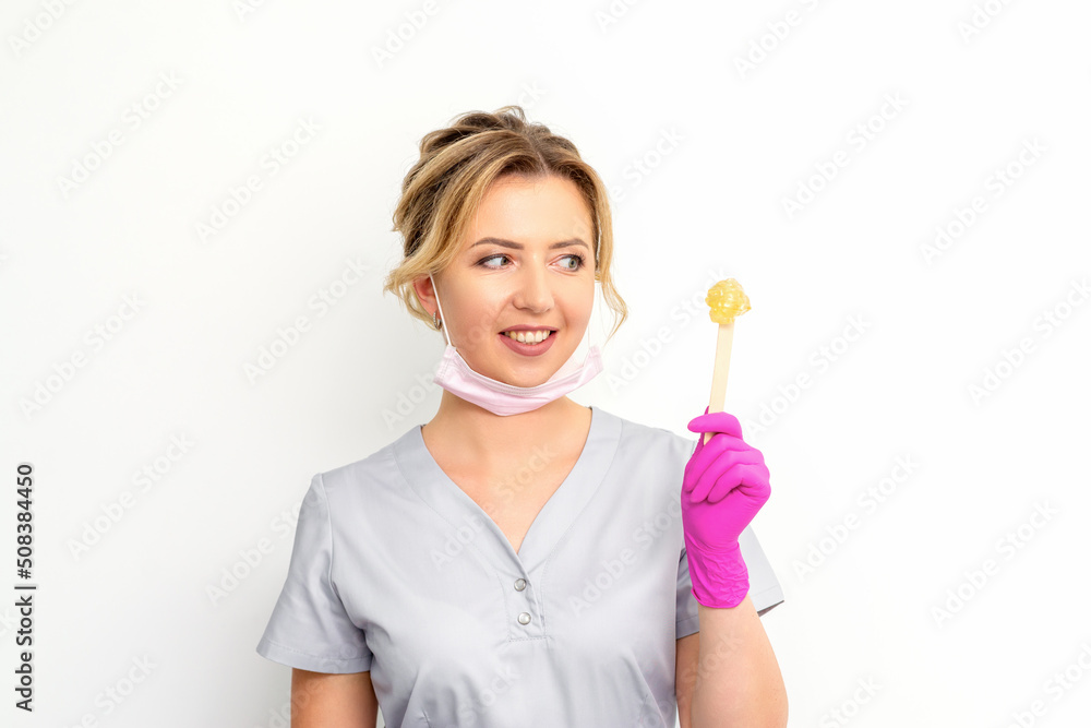 The master of sugar hair removal holds liquid yellow sugar paste, wax for depilation on a wooden stick on a white background The master of sugar hair removal holds liquid yellow sugar paste, wax for depilation on a wooden stick on a white background