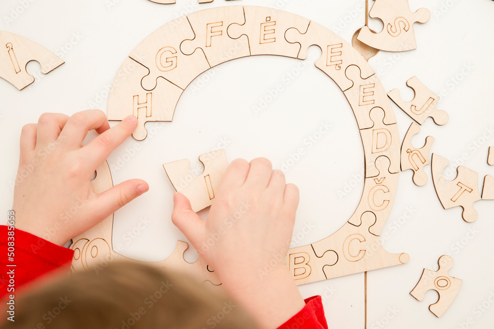 3D wooden toy. Learning letters in order of alphabet. Child's fingers holds pieces of unfinished to assemble puzzle. 3D wooden toy. Learning letters in order of alphabet. Child's fingers holds pieces of unfinished to assemble puzzle.
