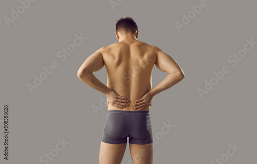 Naked man in underwear on grey background suffer from backache or spasm. Pain in lower spine. Guy struggle with painful feeling in back, have kidney stones or inflammation. Healthcare concept.