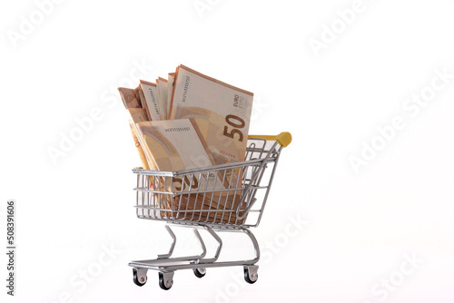 Toy supermarket cart or shopping trolley with money isolated on white background close-up.