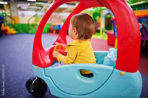 Cute baby girl rides on a plastic car in indoor play center.