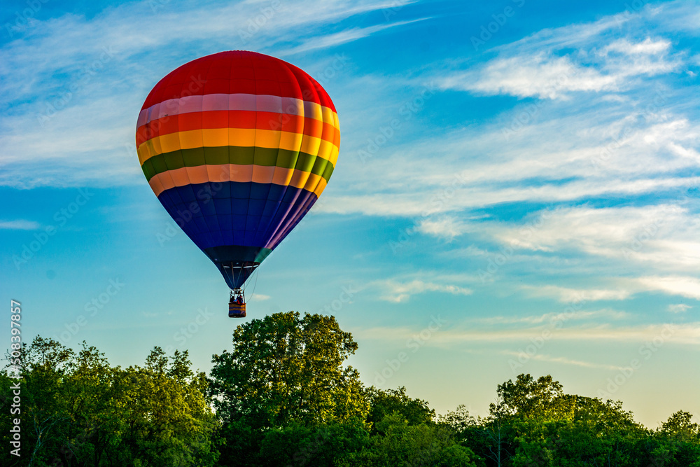 Hot Air Balloon over the trees with white clouds and golden sunset Hot Air Balloon over the trees with white clouds and golden sunset