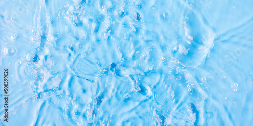 Rippling water surface and droplet on blue background close view from above