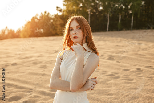 Foto Charming redhead woman with long hair touching chin and looking at camera on san