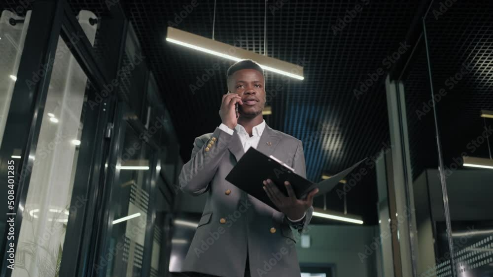 A black man is talking on the phone and walking down the corridor with documents A black man is talking on the phone and walking down the corridor with documents